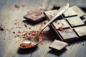 Cocoa Powder on spoon and Dark Chocolate background.